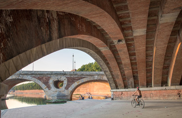 homme faisant du vélo sur des quais et passant sous un vieux pont 