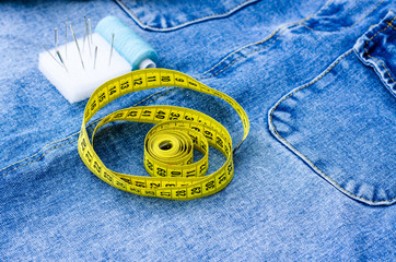 There are sewing supplies on top of the denim items. A centimeter, threads, pins and a thimble lie on things. Cutting and sewing concept.