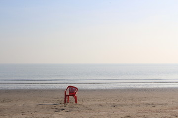 Fototapeta na wymiar red plastic chair at a calm and empty beach