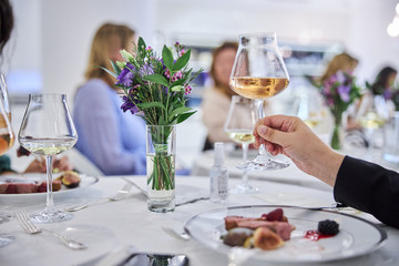 hand is holding glass of white wine in vip restaraunt
