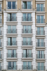 Fragment of modern facade with big windows and curtains and wrought iron fences decorated with forged patterns, vertical photo