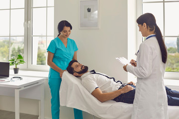 Obraz premium Young doctor and her assistant working with male patient at clinic. Medical specialists helping their client at hospital