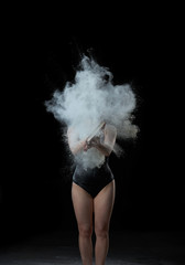 young beautiful woman in a black textile bodysuit holds a book in her hands, cloud of white wheat flour flies out of the book