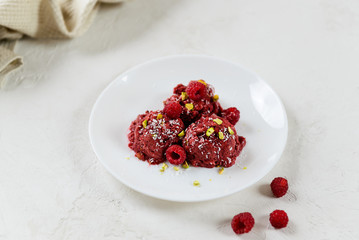 Homemade raspberry ice cream from aquafaba with pistachios and coconut on a white plate.