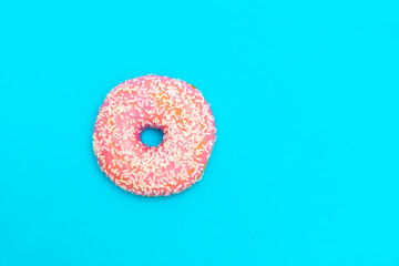 Pink glazed donut with sprinkles on blue background. Image with copy space, top view
