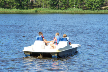 Three children in life jackets ride a catamaran in a clean, transparent lake