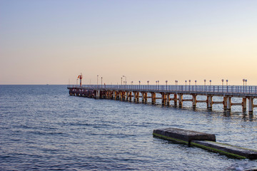 Fototapeta na wymiar Sea in the evening. The pier goes off into the distance. Dark blue sky and water.Concrete blocks and breakwaters are visible.