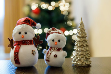 Christmas installation indoor at table of two smart snowmen and christmas tree. Christmas toys, the symbol of Christmas Eve, Advent.  
