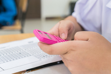 Student using calculator for used making mathematical calculations in exercise taking exam at school or university, taking in assessment paper on education study.