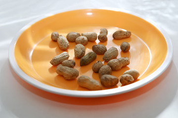 Raw peanuts top view isolated on orange plate at white background with sun rays shadow