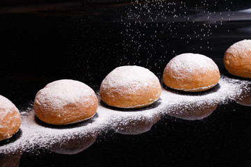 Baking on a black background. White buns sprinkled with powder and flour.