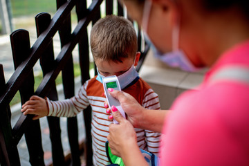 A mom checks her son's temperature with a temporal thermometer. They are going to kindergarten