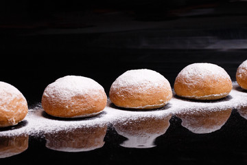 Baking on a black background. White buns sprinkled with powder and flour.