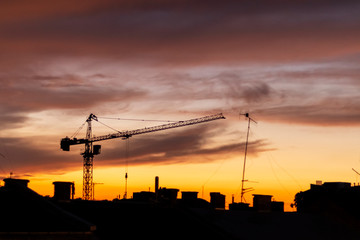 Dark silhouette of city roofs and construction crane on night sky background.