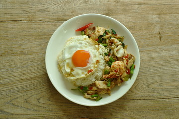 spicy fried seafood and meat chili and herb on rice topping egg in plate