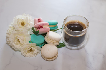 Fototapeta na wymiar Colourful macaroons are laying on the table along with the coffee in transparent cup and white roses, breakfast time. High quality photo