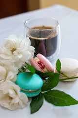 Colourful macaroons are laying on the table along with the coffee in transparent cup and white roses, breakfast time. High quality photo