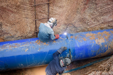 Two workers are connecting underground sewers at a construction site to repair the water pipes by...