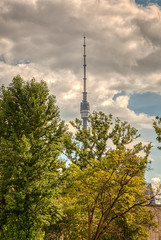 Obraz premium The main Moscow TV tower in Ostankino. Ostankino TV tower on the background of a summer storm sky through the green crowns of trees. Russia, Moscow, August 2020