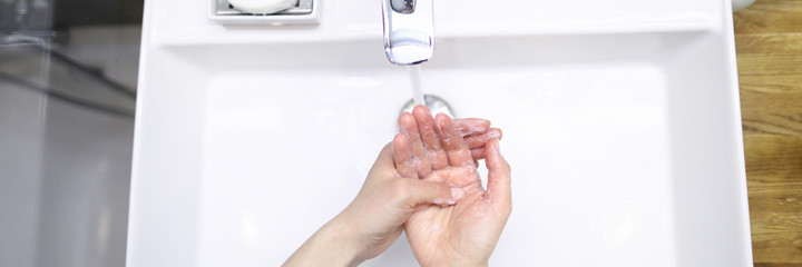 Top view of person washing hands in bathroom using soap. White crane with pouring water. Prevention of infection and virus. Personal hygiene and cleanliness concept