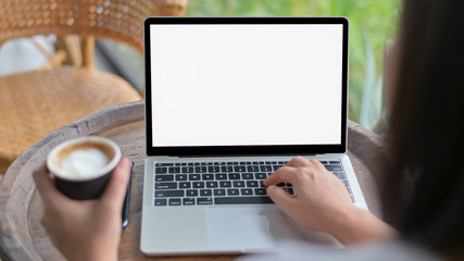 Close-up shot of Woman using a blank screen laptop and holding a coffee mug, Shot from the back.