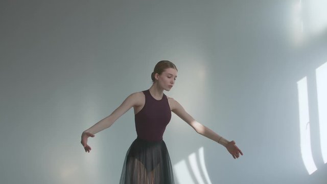 The ballerina performs smooth movements with her hands and dancing in pointe shoes on the tiptoes in rehearsal. Performing in a studio bathed in sunlight. Close up. Slow motion.