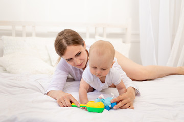 mom playing with baby 6 months lying on a white bed, leisure mom with baby, place for text