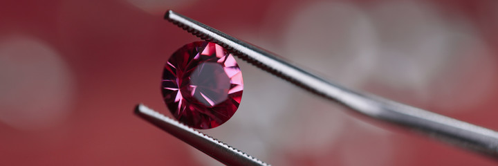 Close-up of beautiful shining crystal. Macro shot of luxury round pink diamond in tweezers. Carat...