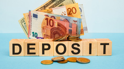 DEPOSIT - word written on wood cubes on the background of various banknotes.