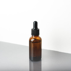 A glass dropper bottle with a pippette with black rubber tip on the grey reflective background. Nature Skin concept. Organic Spa Cosmetics. Close up.