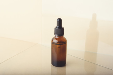 A glass dropper bottle with a pippette with black rubber tip on the beige glass reflective background. Nature Skin concept. Organic Spa Cosmetics. Close up.