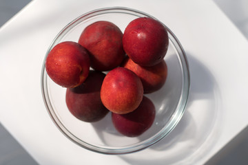 Ripe red plum-peach, nectarine in a glass container on a white background with a play of shadows