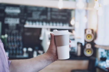 mock-up of a cardboard glass for coffee in a man's hand against the background of a bar in a cafe.