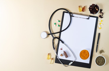 Alternative medicine, nathuropathy or ayurveda concept. Blank clipboard with stethoscope, various healing herbs, spices, capsules and healthy oils on beige table top view