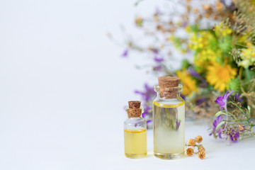 Bottles of organic essential oil with fresh and dried healing herbs and flowers on white table