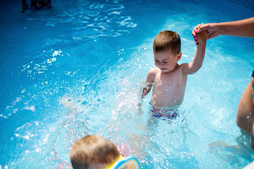 Fototapeta na wymiar Little boys and his mother having fun in swimming pool at back yard