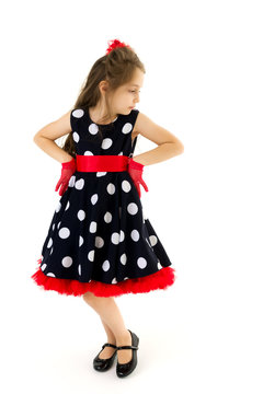 Charming Girl in Blue Polka Dot Dress Standing with Hands on Her