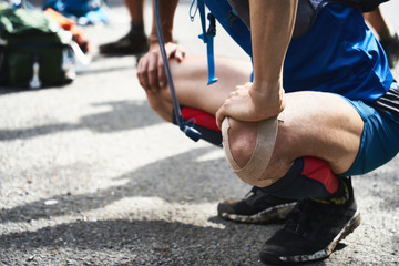男性のトレイルランナーがトレーニングの前にストレッチしている姿。膝をキネシオテープでテーピング。