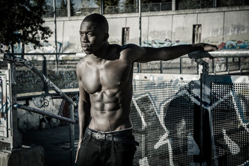 Fototapeta na wymiar Portrait of a hot muscular young black man shirtless in urban environment, walking on metal stairs, looking at camera