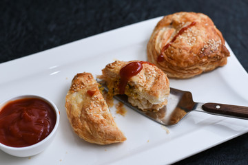Fast food many chicken puffs, pattie pastries, popular bakery snacks with tomato sauce or ketchup in Kerala India. Indian food cut and being served using server.