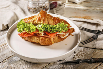 Close-up croissant with ham, cheese, tomato and fresh salad on a white plate. Morning food still life. Tasty breakfast