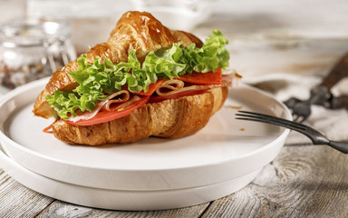 Croissant with ham, cheese, tomato and fresh salad on a white plate. Morning food still life. Tasty breakfast