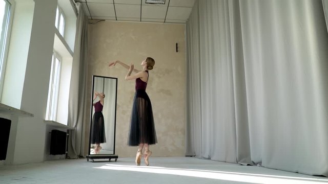 Beautiful girl dancer performs classical ballet in the loft design Studio with large white panoramic windows. Young ballerina rehearsal in front of the mirror.