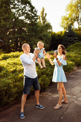 Fototapeta premium Happy mom and dad play with cute daughter, smiling, lovely parents with little baby girl at the park, caring father lift in air beautiful toddler, enjoy family moments concept