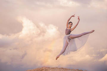 ballerina in a light long dress soars above the ground like a bird in a jump against the background...