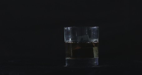 In front of a black background, whiskey is poured into a glass of whiskey stones.