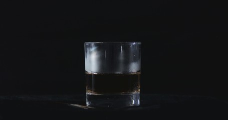In front of a black background, whiskey is poured into a glass