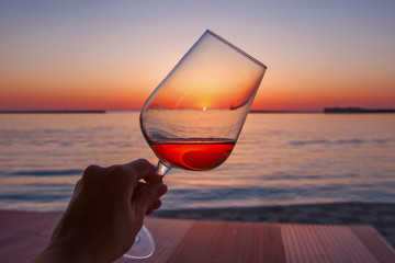 A glass of wine in the hand of a woman against the background of the sea. Beautiful sunset by the sea. The sun in a glass of wine.