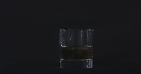  On a black background, ice falls into a glass of whiskey