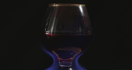 A glass of red wine on fire stands on a beautiful natural stone